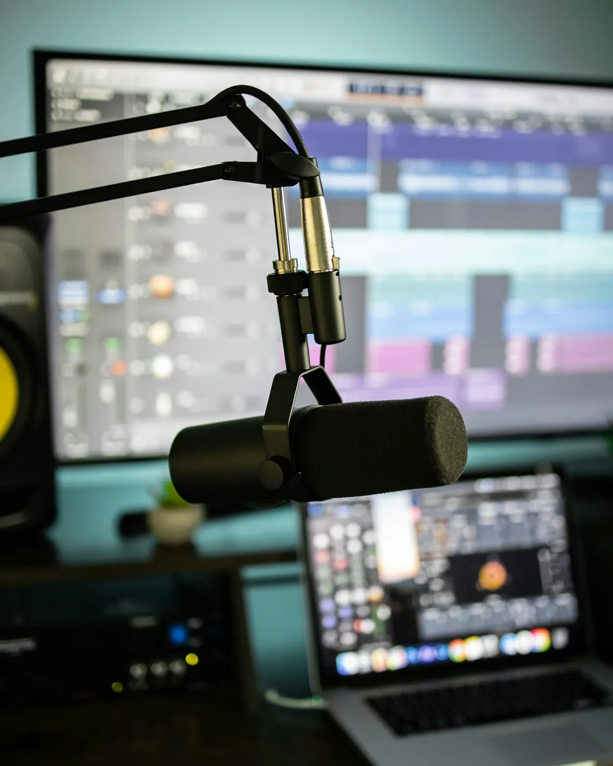 A studio microphone in front of a monitor and laptop in a creator's workspace.